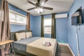 A bedroom with a bed, a ceiling fan, a window with curtains, a flat-screen TV mounted on the wall, and a bedside table. - Near Texans | NRG Stadium | Med Center | Downtown! (Houston)