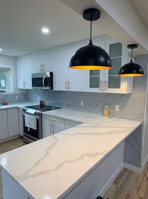 A modern kitchen with white cabinetry, a stainless steel oven, a microwave, and a marble countertop.