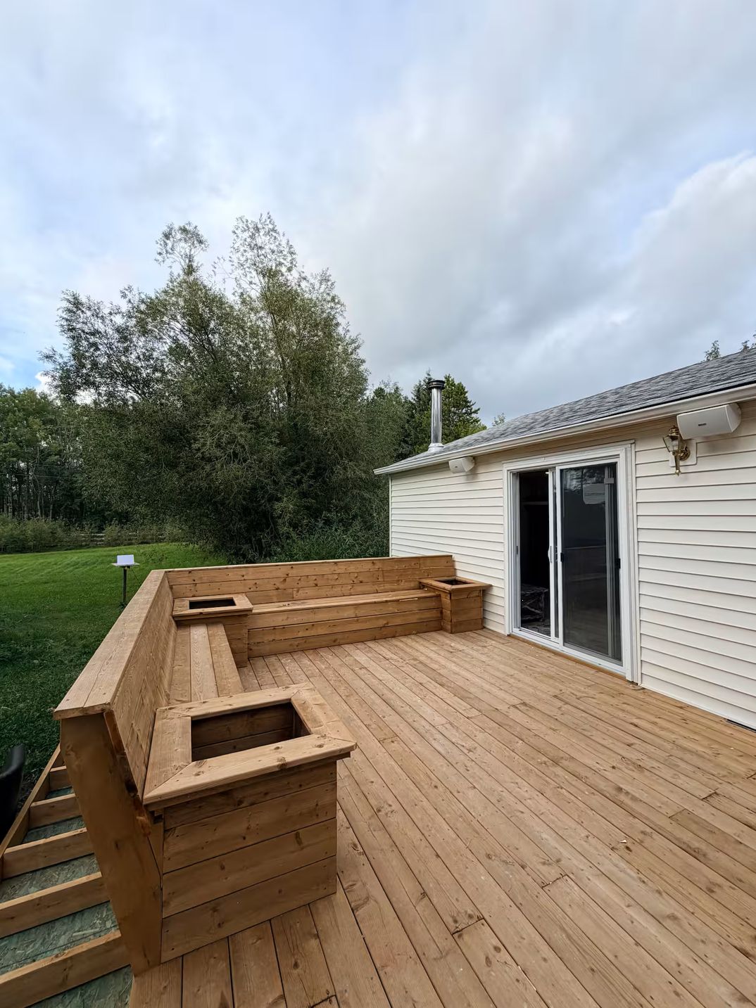 Una terraza de madera con asientos integrados y una chimenea, junto a una casa con puerta corrediza de vidrio.