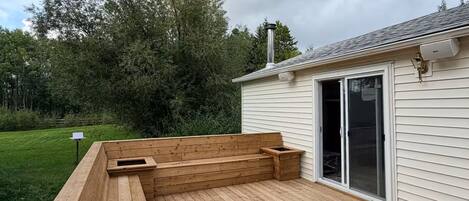 Una terraza de madera con asientos integrados y una chimenea, junto a una casa con puerta corrediza de vidrio.