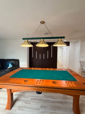 A pool table in a room with a dark wall and a green accent wall. There is a hanging light fixture above the table.