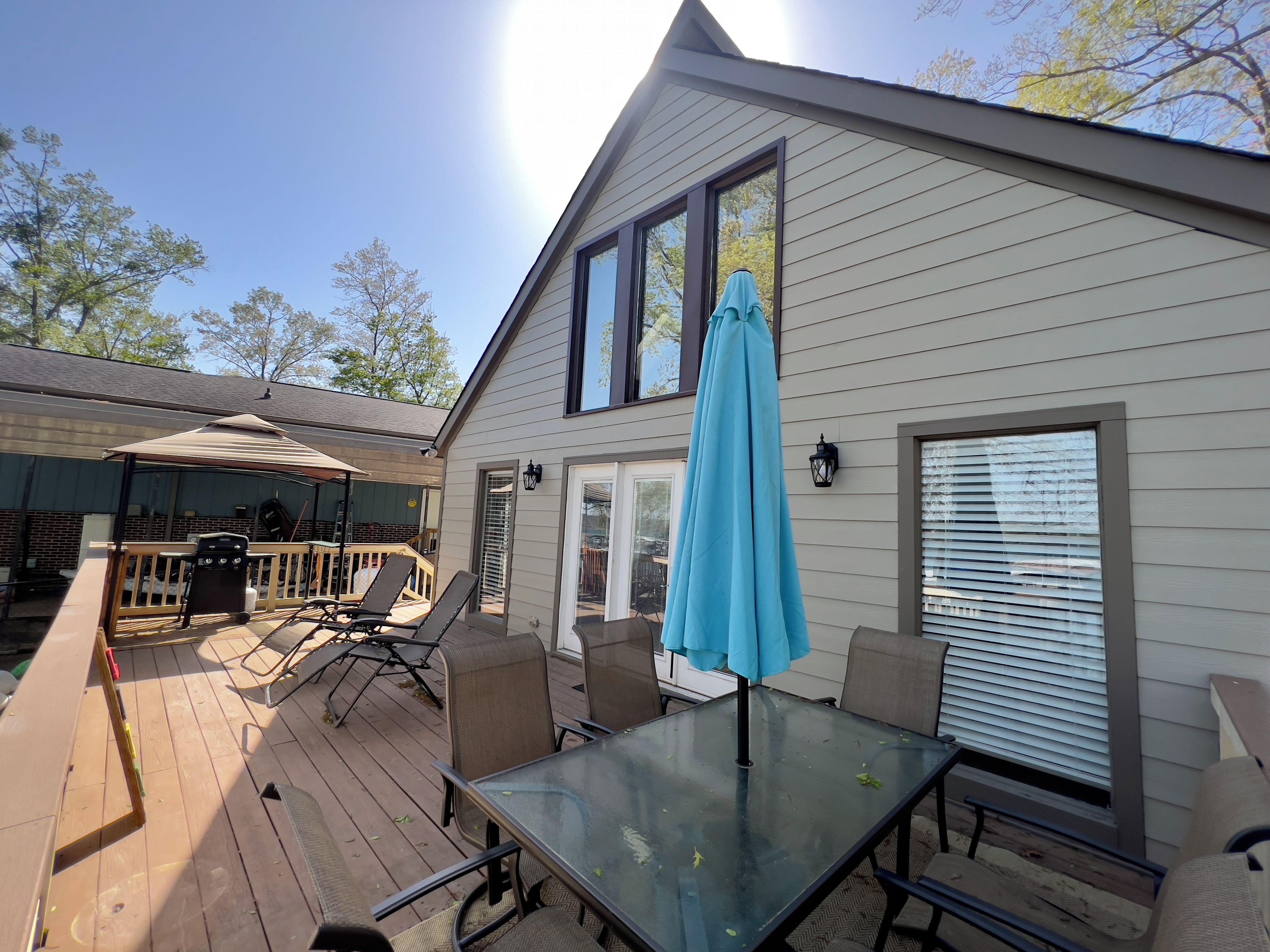 A deck with outdoor furniture, a glass table, and a blue umbrella.