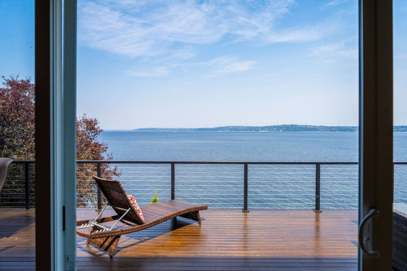 A wooden deck with a lounge chair and a view of a large body of water.