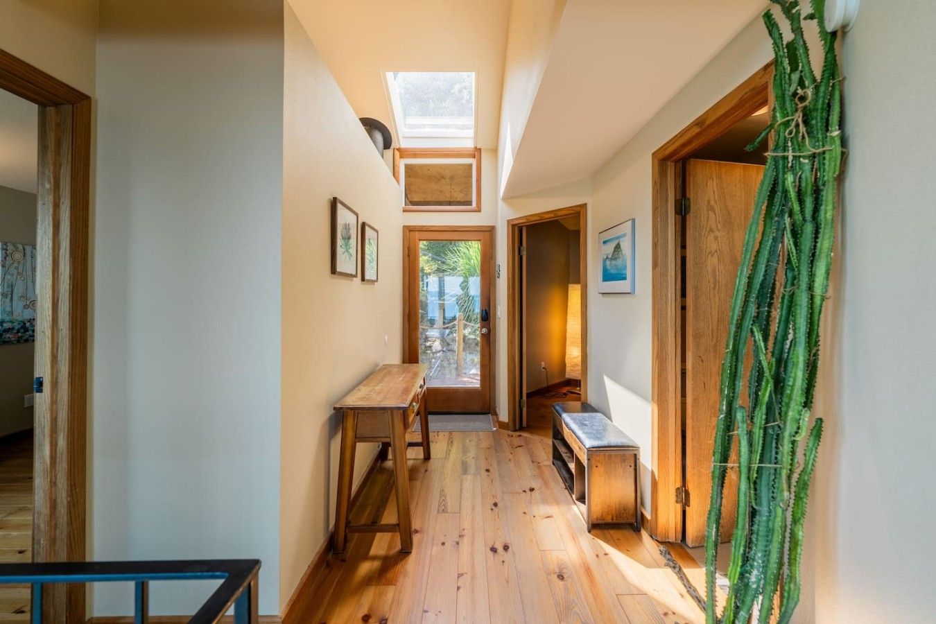 Um corredor estreito com piso de madeira, um banco e uma porta que dá para um quarto claro com claraboia.