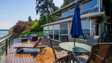 A wooden deck with outdoor furniture, a glass-enclosed room, and a view of the water.