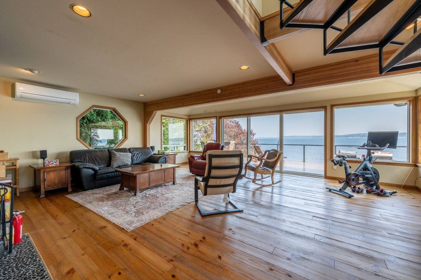 Un ampio soggiorno con una grande finestra vista acqua, pavimento in legno e soffitto con travi a vista.