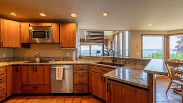 A kitchen with wooden cabinets, a stainless steel refrigerator, a built-in oven, a dishwasher, and a large window offering a view of the outdoors.
