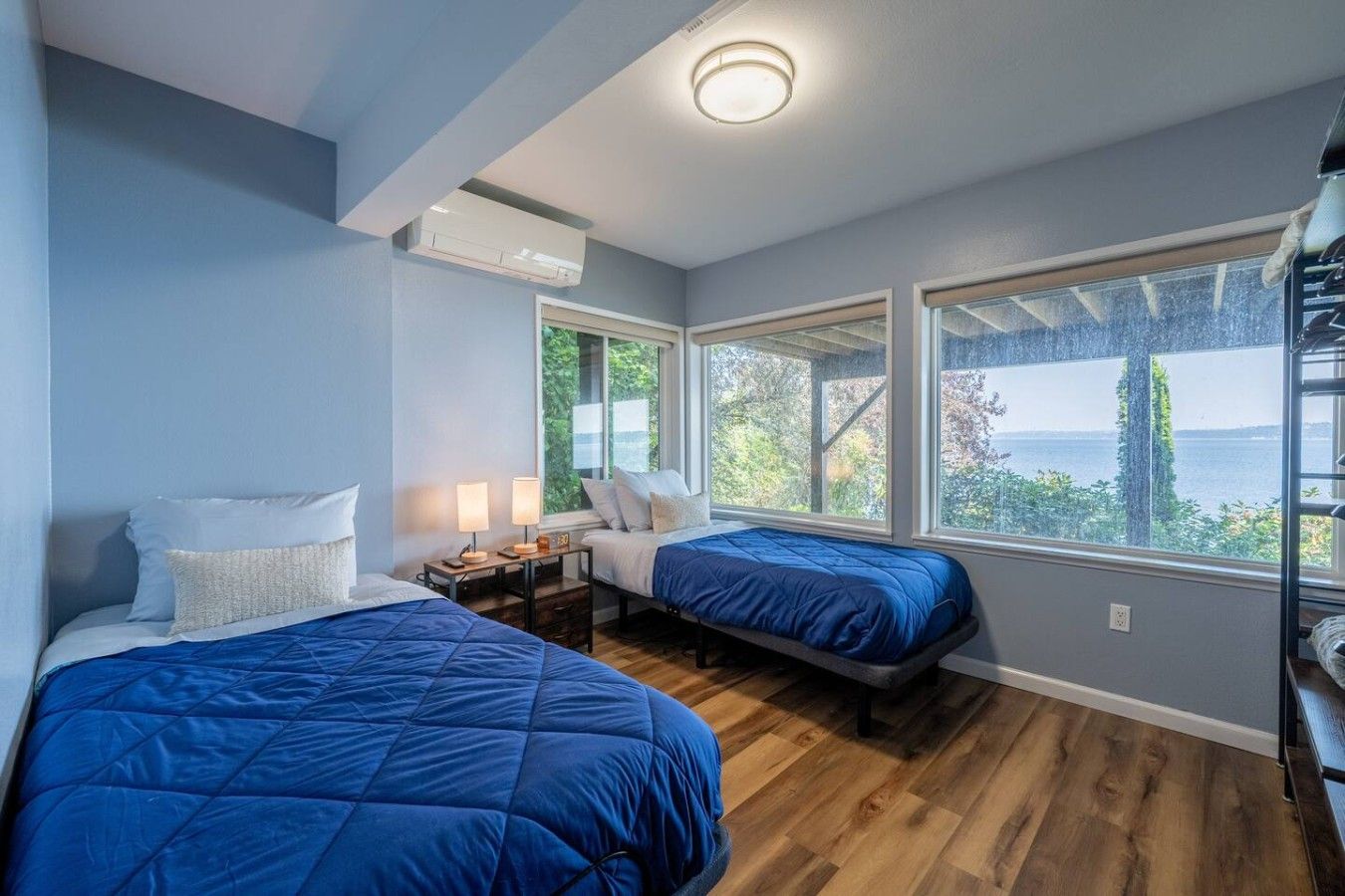 Quarto com duas camas, mesa de cabeceira, abajur e janelas amplas com vista para o exterior.