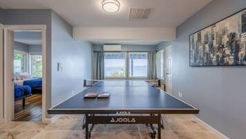 A room with a table tennis table, a bed with blue bedding, and a cityscape painting on the wall.