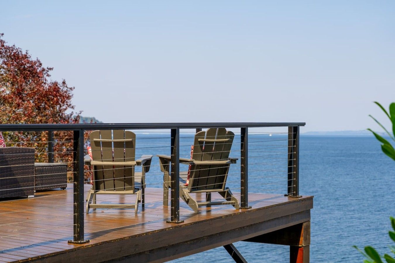 A deck with two Adirondack chairs facing a body of water.