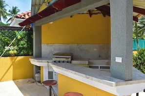 Un área de cocina al aire libre con estufa a gas, pileta y mostrador tipo barra.
