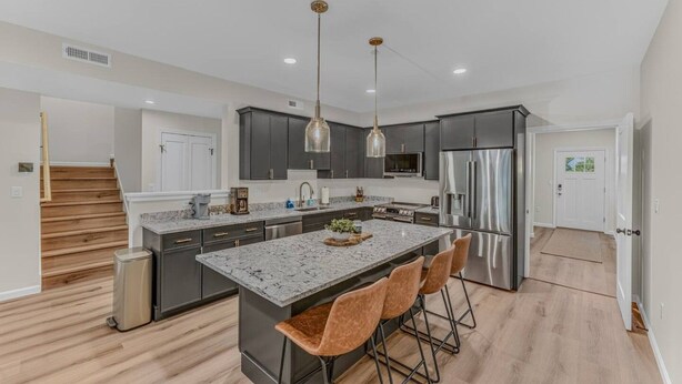 A modern kitchen with dark cabinets, stainless steel appliances, and a central island with bar stools. - Soulful Summit at Forest Ridge- Pools & Hot Tub (Lincoln)