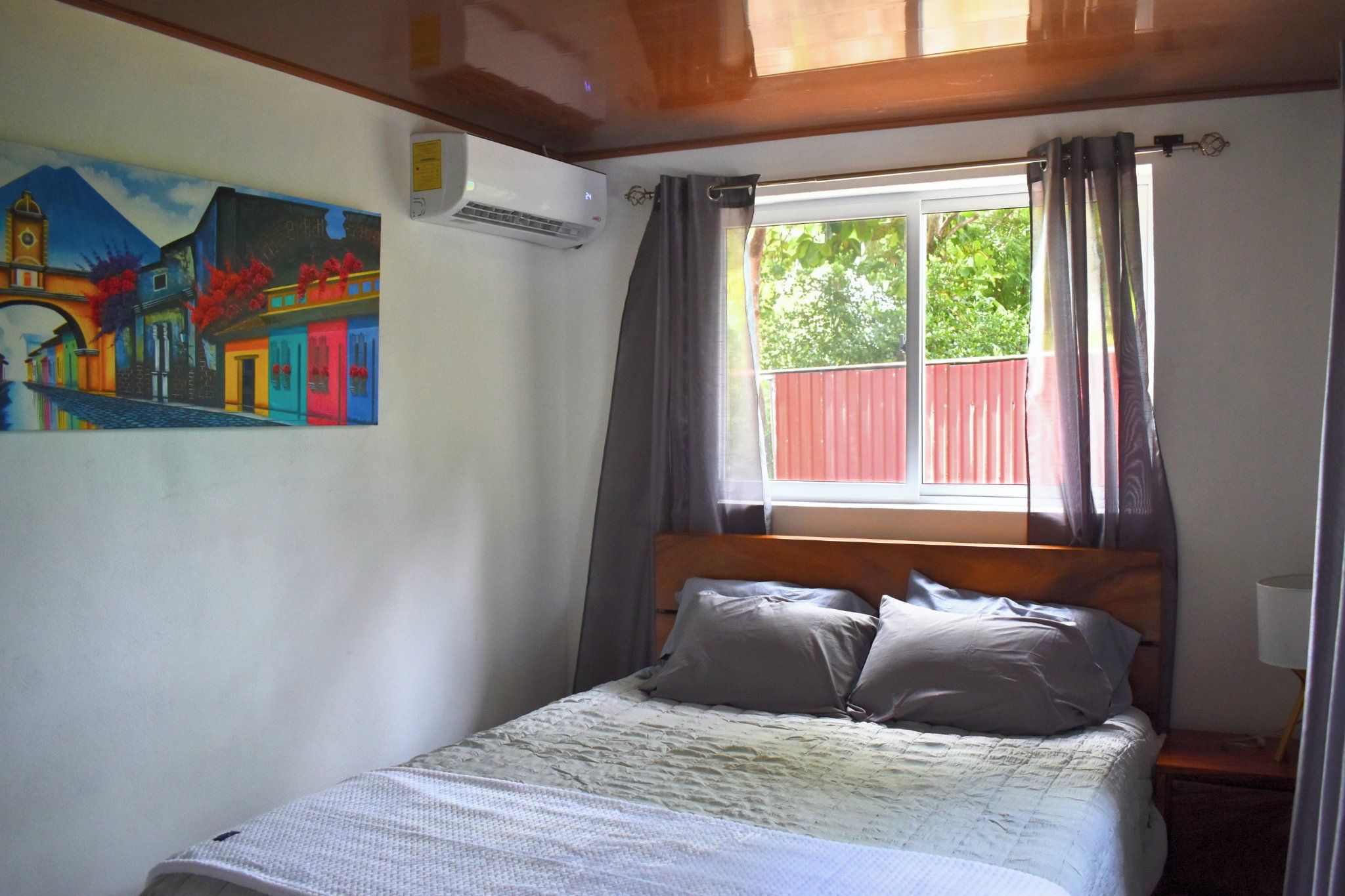 Ein Schlafzimmer mit einem Bett, einem Gemälde, einer Klimaanlage und einem Fenster mit Vorhängen.