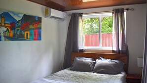 Ein Schlafzimmer mit einem Bett, einem Gemälde, einer Klimaanlage und einem Fenster mit Vorhängen.