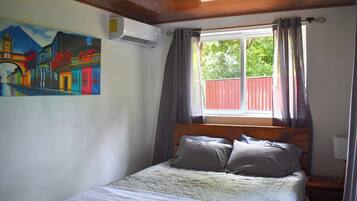 Ein Schlafzimmer mit einem Bett, einem Gemälde, einer Klimaanlage und einem Fenster mit Vorhängen.