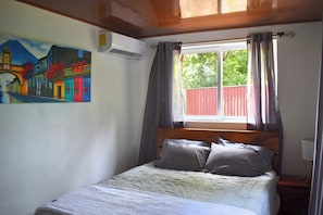 Una camera da letto con un letto, un quadro, un condizionatore d'aria e una finestra con tende.