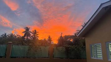 Pôr do sol com céu limpo, palmeiras e um edifício com portão.