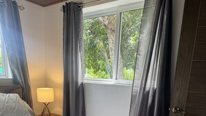 Ein Schlafzimmer mit einem Bett, einem Nachttisch, einer Lampe und einem Fenster mit Vorhängen.