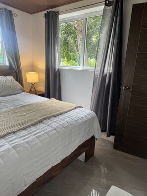 Una camera da letto con un letto, un comodino, una lampada e una finestra con tende.