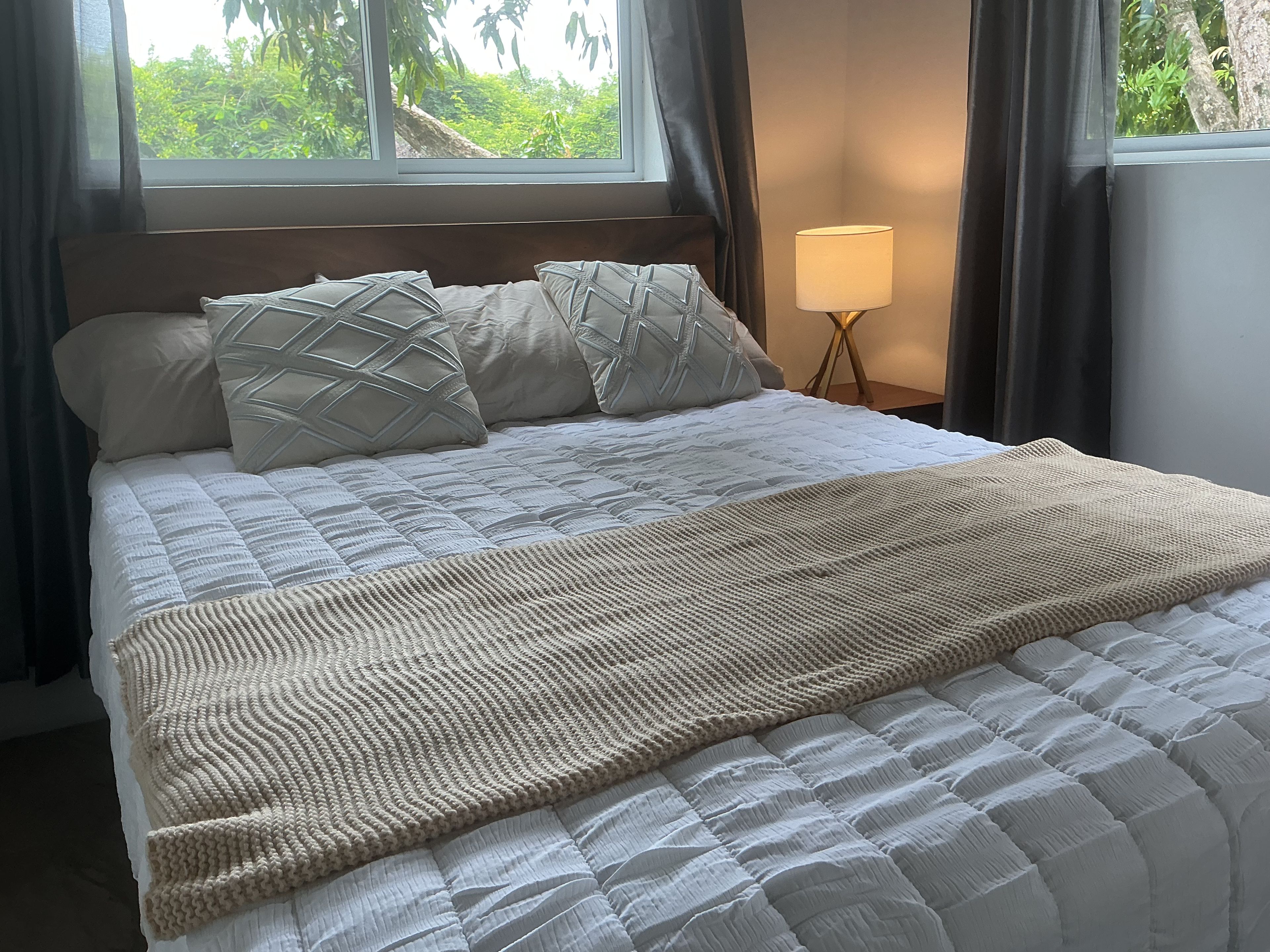 Ein Bett mit einer gesteppten weißen Daunendecke, zwei gemusterten Kissen und einer gestrickten Tagesdecke.