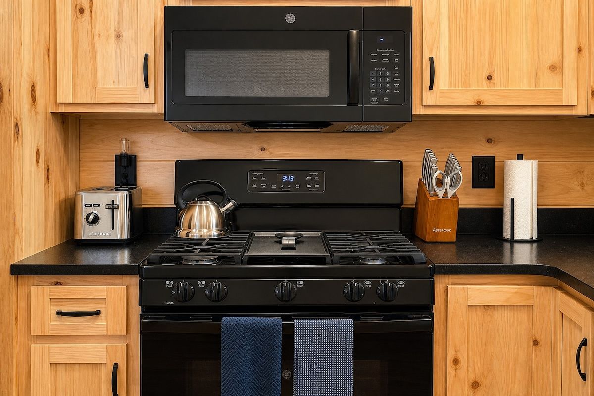 A kitchen with wooden cabinets, a microwave, a gas stove, a toaster, and a kettle.
