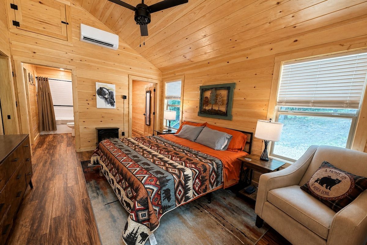 Une chambre dans une cabane en bois, avec un lit, une chaise, une table de chevet et une fenêtre.