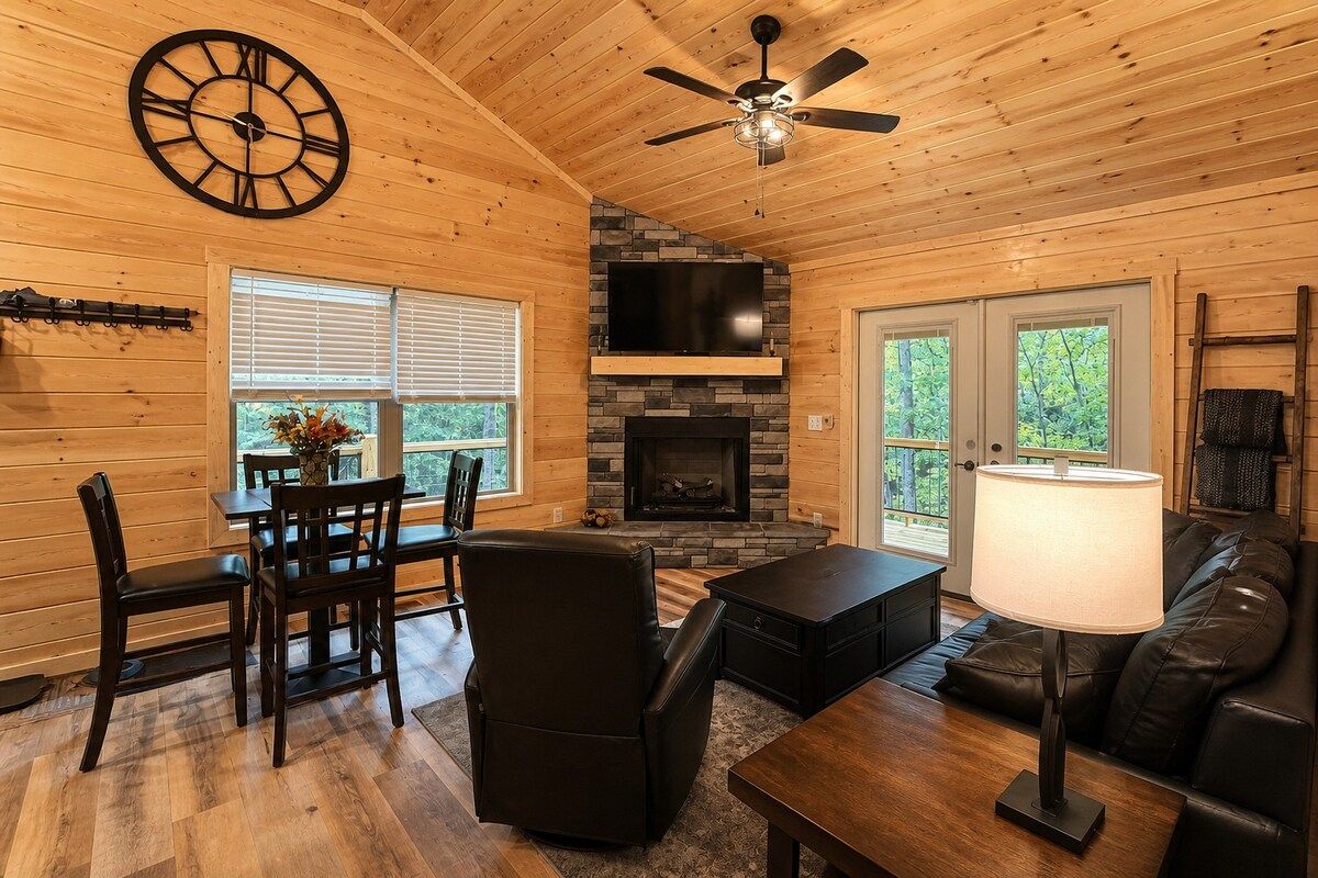 A wooden interior with a fireplace, a ceiling fan, a clock, and a dining area.