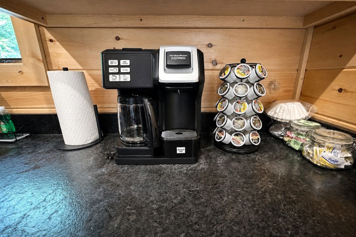 Una cafetera, un dispensador de toallas de papel y un dispensador de granos de café sobre una encimera.