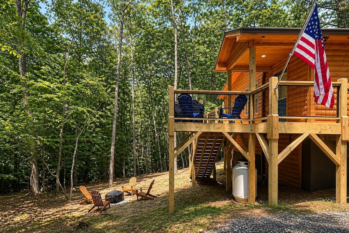 A wooden cabin with a deck, an American flag, and a large window.