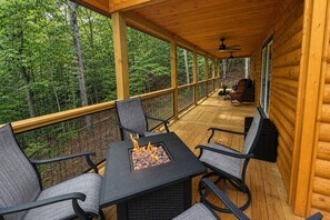 Una terraza techada con una mesa y sillas alrededor de una fogata, rodeada por un bosque.