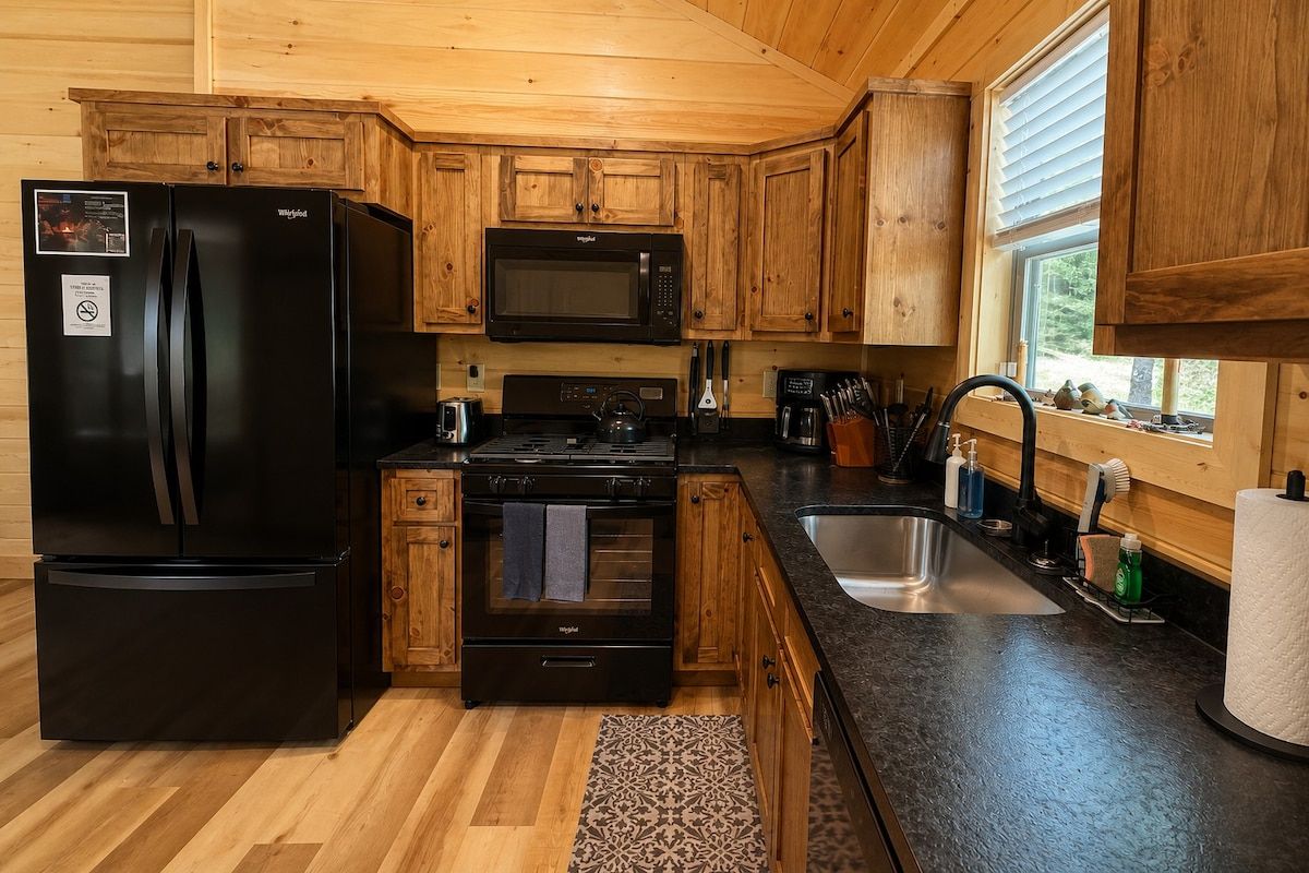 Una cocina compacta con armarios de madera, un refrigerador negro, un microondas, un horno y un lavamanos.