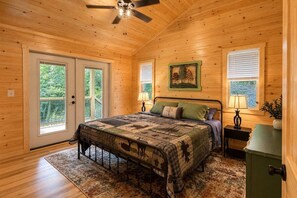Un dormitorio con paneles de madera, una cama, dos ventanas, un ventilador de techo y una puerta.