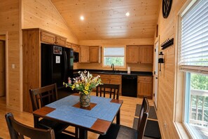 Un interior de madera con una mesa de comedor, sillas, un refrigerador y una ventana con persianas.