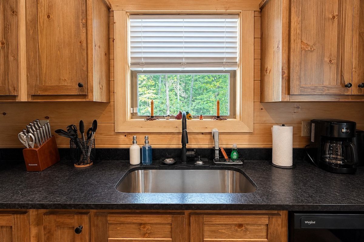 A kitchen with wooden cabinets, a stainless steel sink, and a window with blinds.