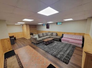 A living room with a sectional sofa, a coffee table, a patterned rug, and a wooden accent wall. - Pet friendly ski chalet 5min from Sunday River (Bethel)