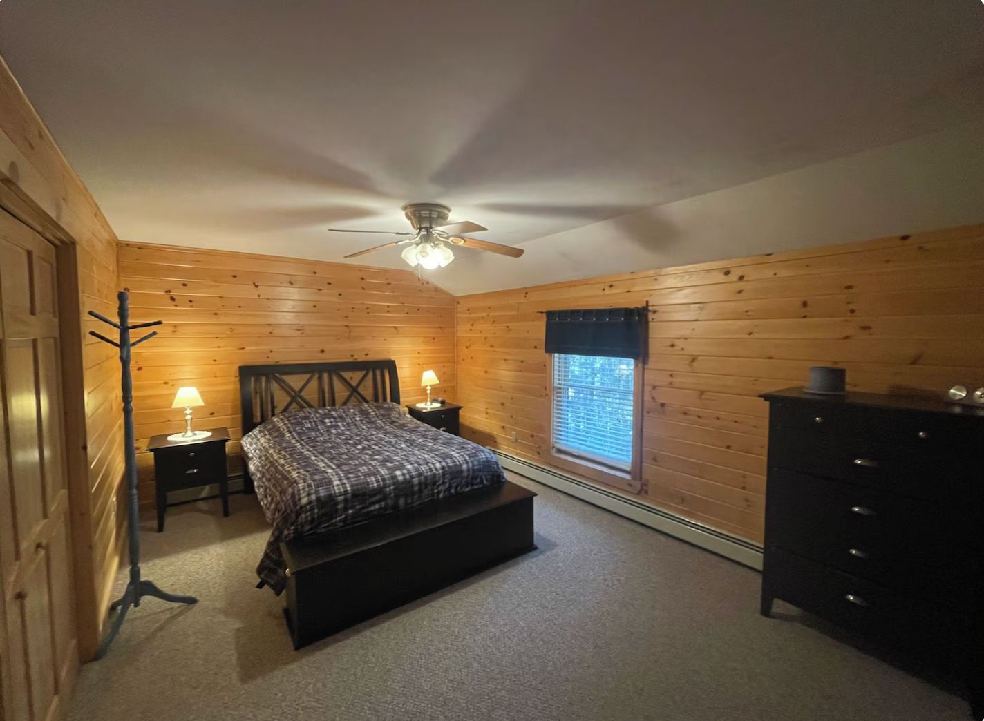 A bedroom with a bed, a dresser, a window with blinds, a ceiling fan, and a coat rack.