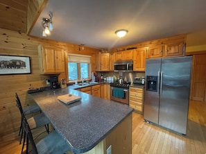 A kitchen with wooden cabinets, a granite countertop, stainless steel appliances, and a dining area with chairs. - Pet friendly ski chalet 5min from Sunday River (Bethel)