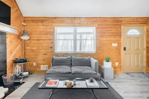A cozy room with a wooden wall, a sofa, a coffee table, and a door. - The Pine Haven - 8 Min to Kalahari - Hot Tub & Fire Pit (Long Pond)