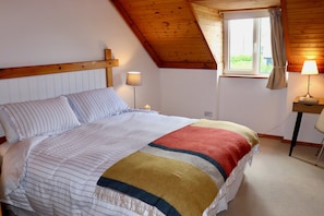 A bedroom with a bed, a nightstand, a lamp, and a window with curtains. - Waterville Holiday Home (Kerry)