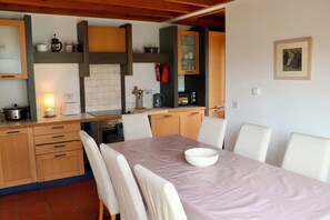 A modern kitchen with wooden cabinets, a dining table with chairs, and a single bowl on the table. - Waterville Holiday Home (Kerry)