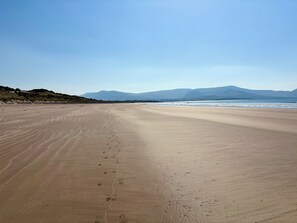 A wide sandy beach with footprints leading towards the water, a clear sky, and distant mountains. - Waterville Holiday Home (Kerry)