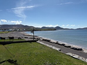 A coastal landscape with a pebble beach, grassy areas, and a clear sky. - Waterville Holiday Home (Kerry)