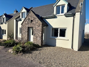 A two-story house with a stone facade, a pitched roof, and a gravel driveway. - Waterville Holiday Home (Kerry)