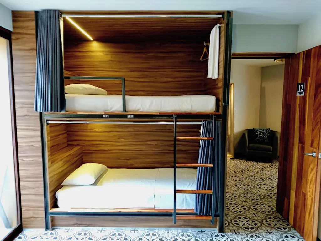 Quarto com beliche, cabeceira de madeira, mesa pequena e piso estampado.