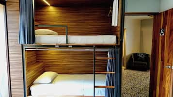Quarto com beliche, cabeceira de madeira, mesa pequena e piso estampado.