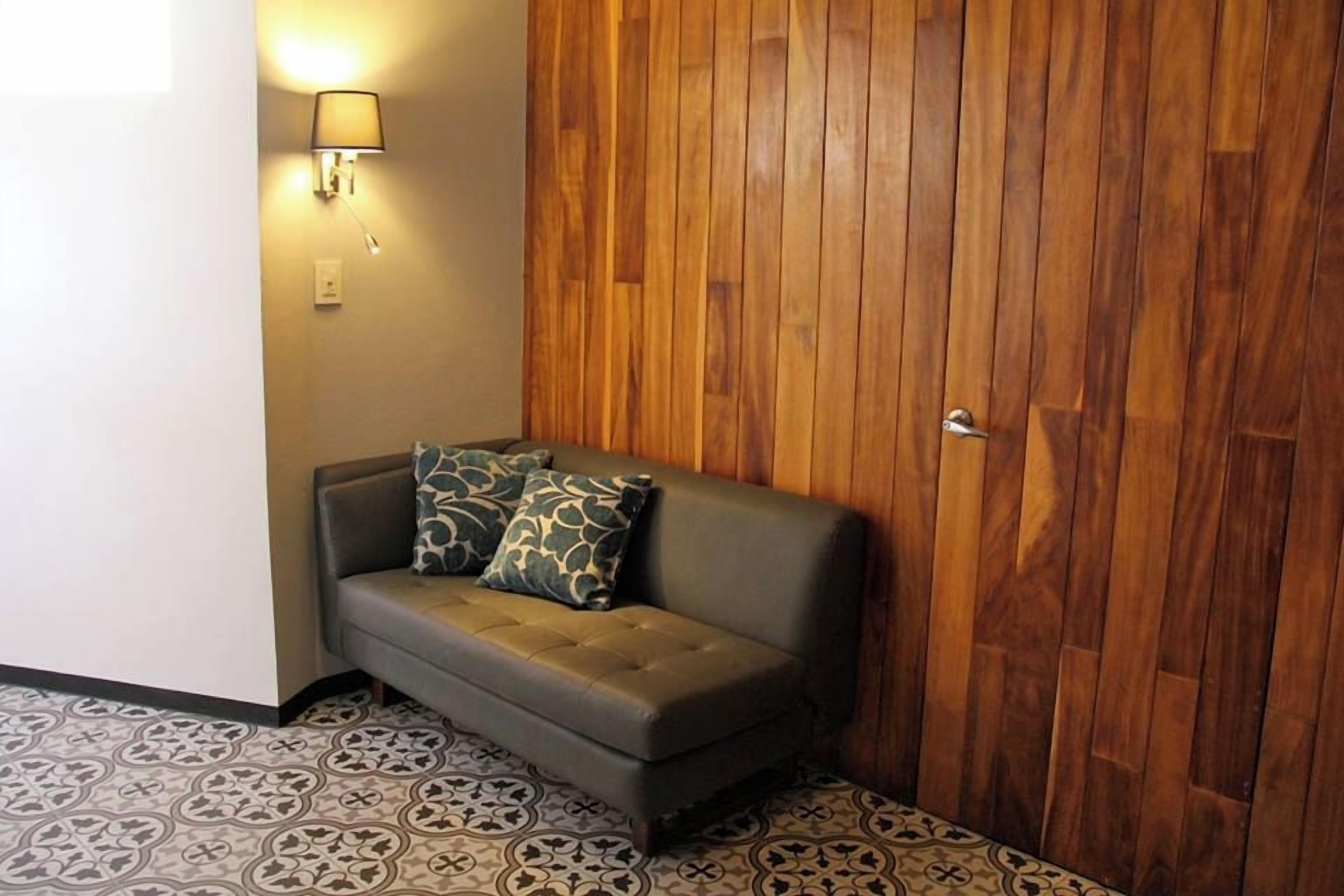 Quarto de canto com sofá, piso estampado, painel de madeira na parede e luminária fixada.