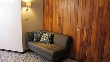 Quarto de canto com sofá, piso estampado, painel de madeira na parede e luminária fixada.