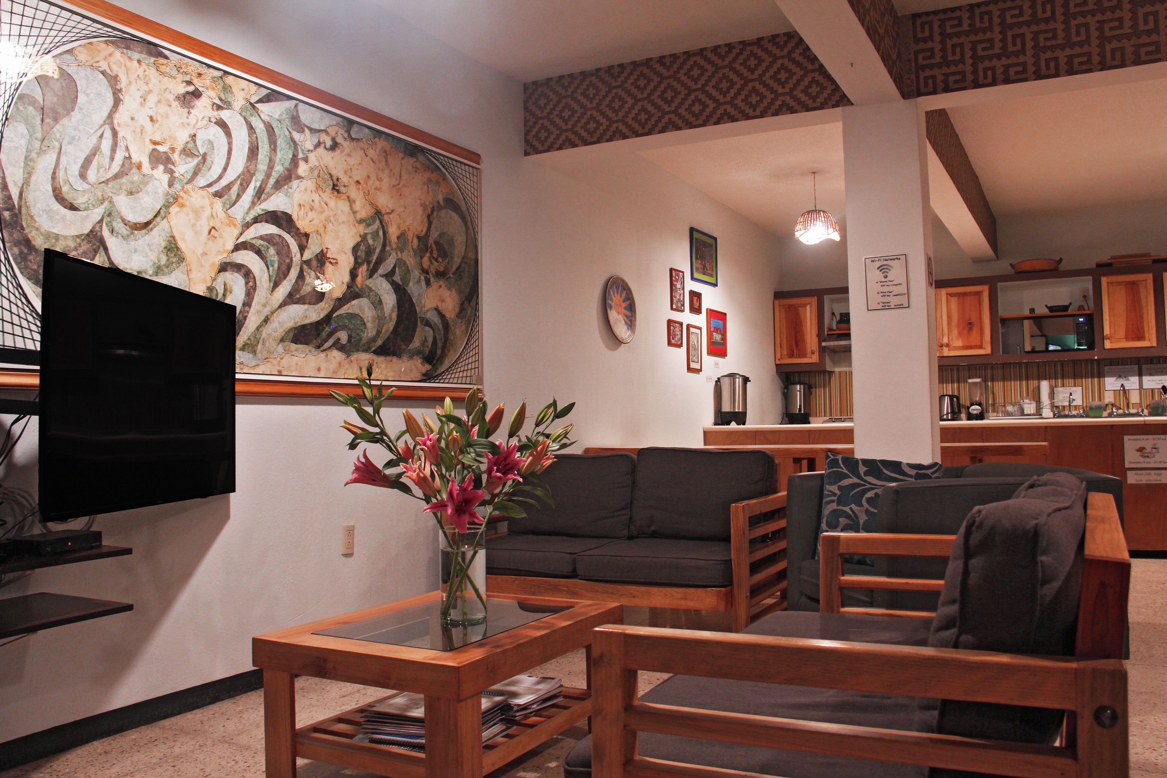 A living room with a flat-screen TV, a coffee table with magazines, a sofa, and a floral arrangement.