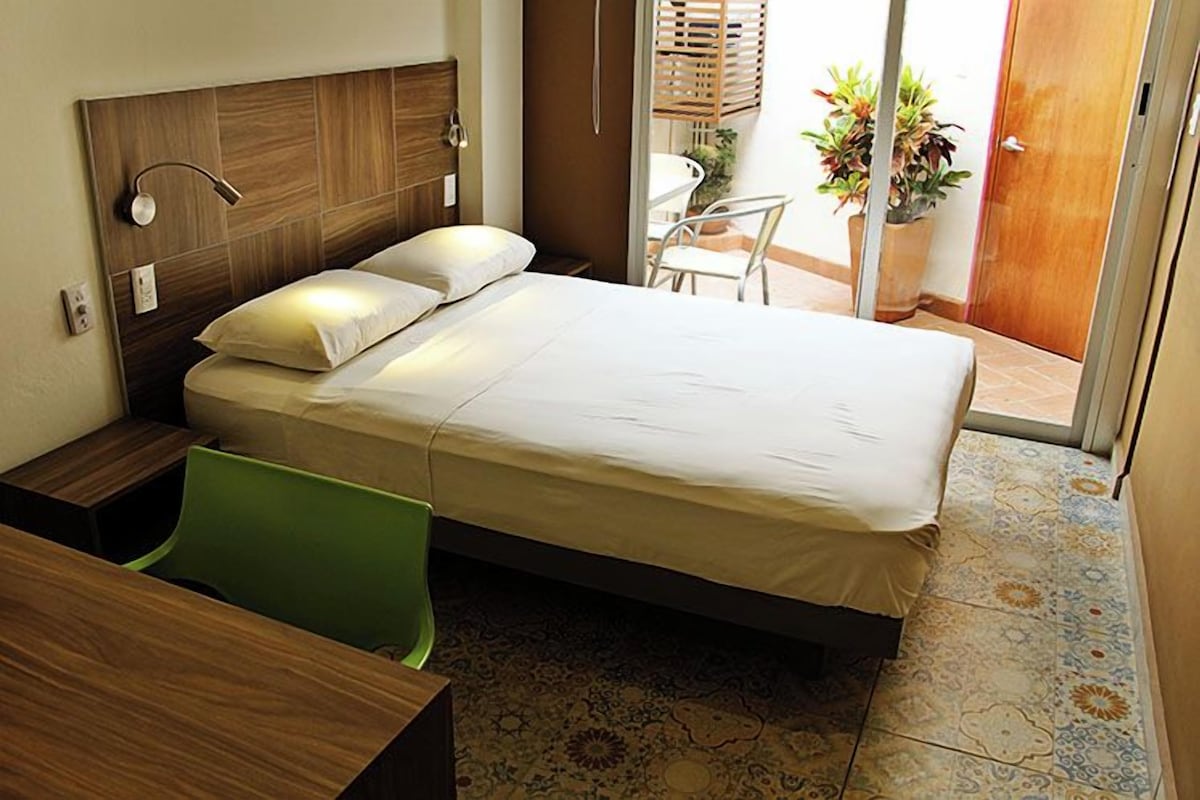 Habitación de hotel con cama, escritorio, una silla y una planta en maceta.