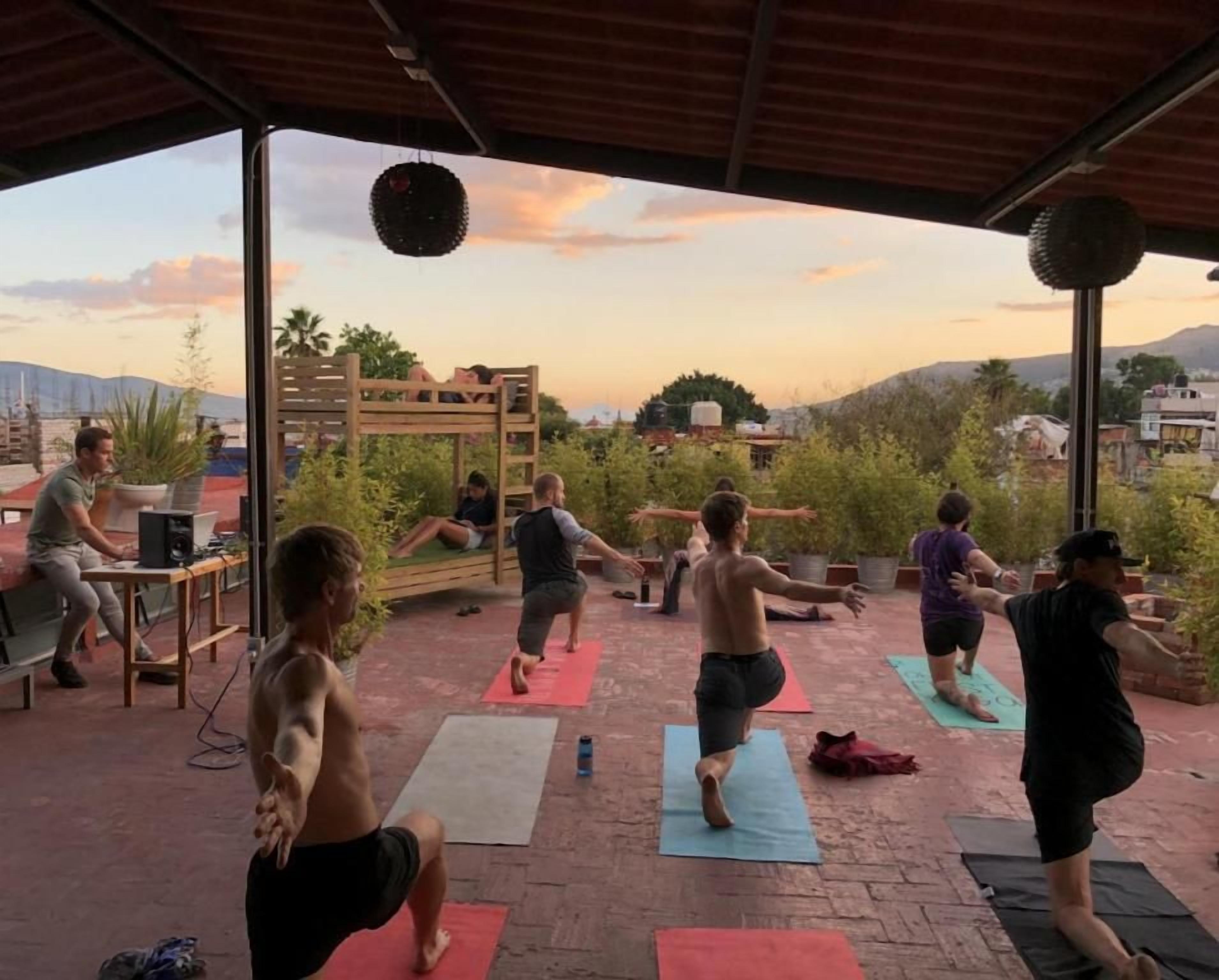 Aula de yoga ao ar livre com participantes em tapetes, uma estrutura de madeira e uma vista panorâmica.